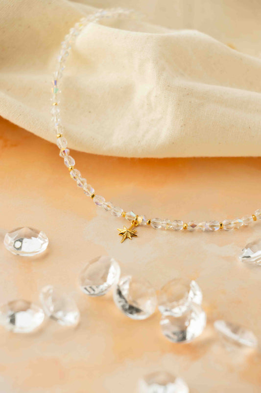 Delicate beaded necklace with a small gold star pendant on a beige fabric background.