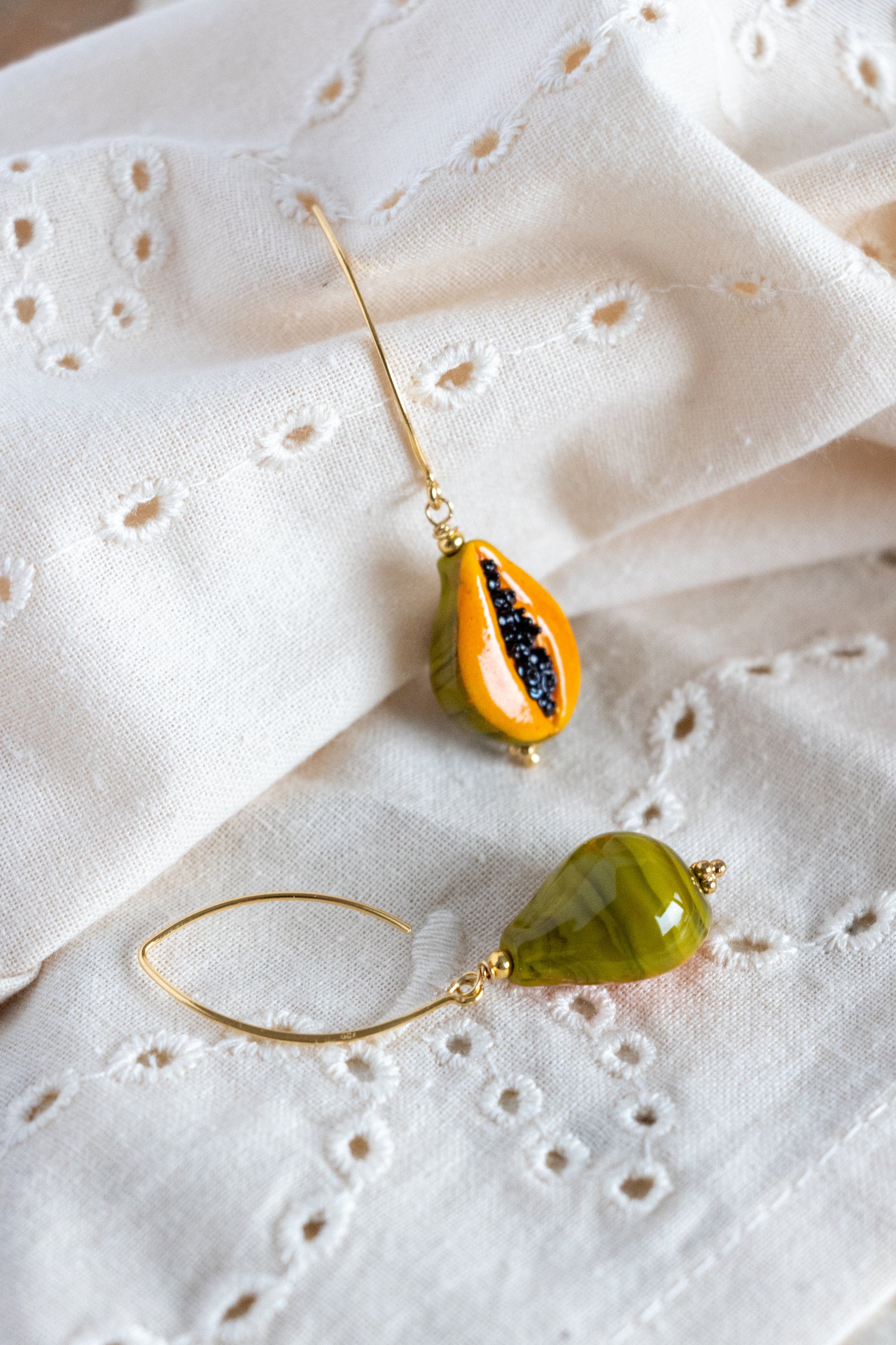 Two teardrop-shaped papaya fruit earrings on a white fabric background