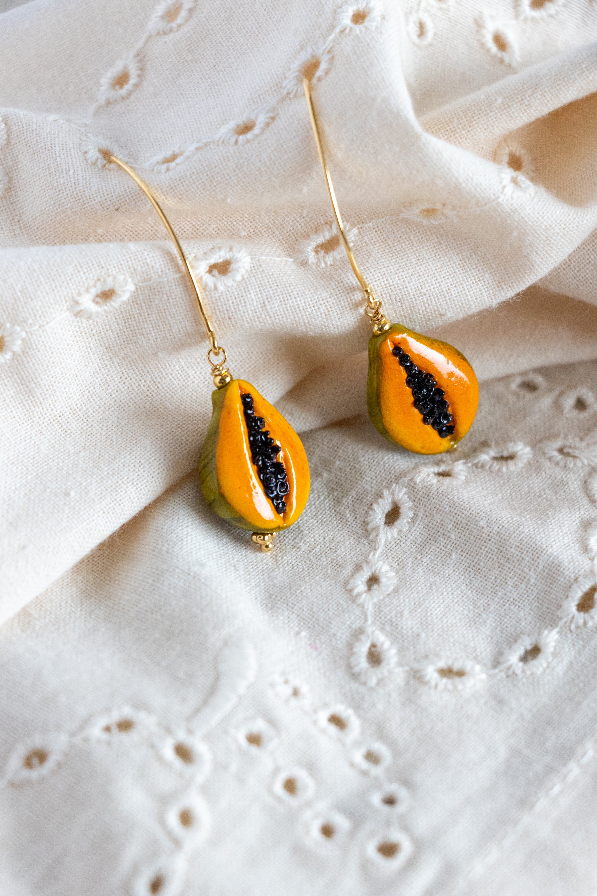 Papaya earrings on a textured white fabric background